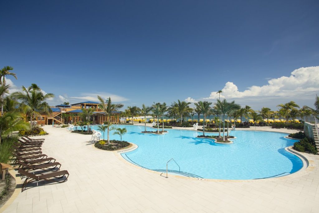 Alt Text:
Harvest Caye resort-style pool with swim-up bar palm trees and Flighthouse lighthouse Belize