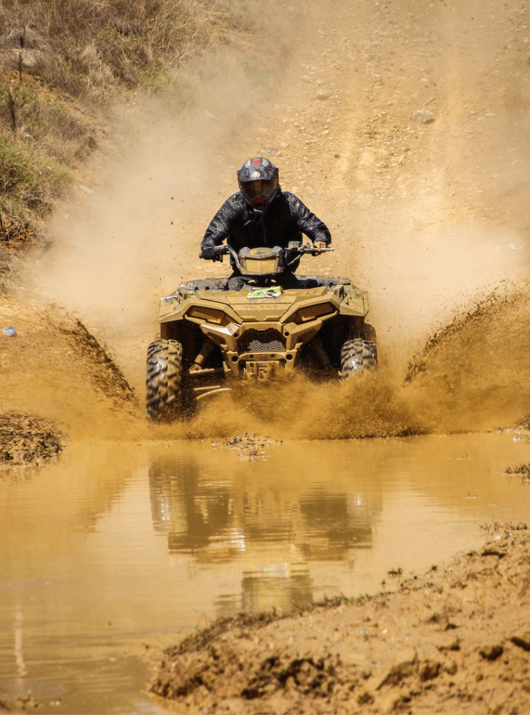ATV rider splashing through mud on an off-road excursion trail