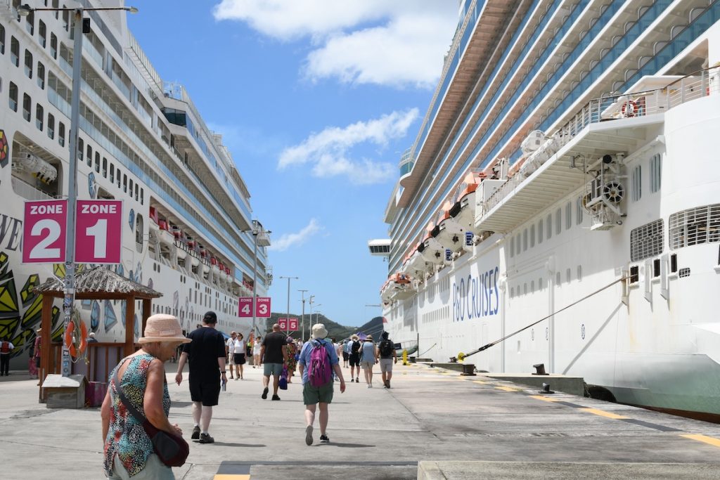 Cruise passengers walking the pier between two large cruise ships at a busy port — the moment situational awareness matters most