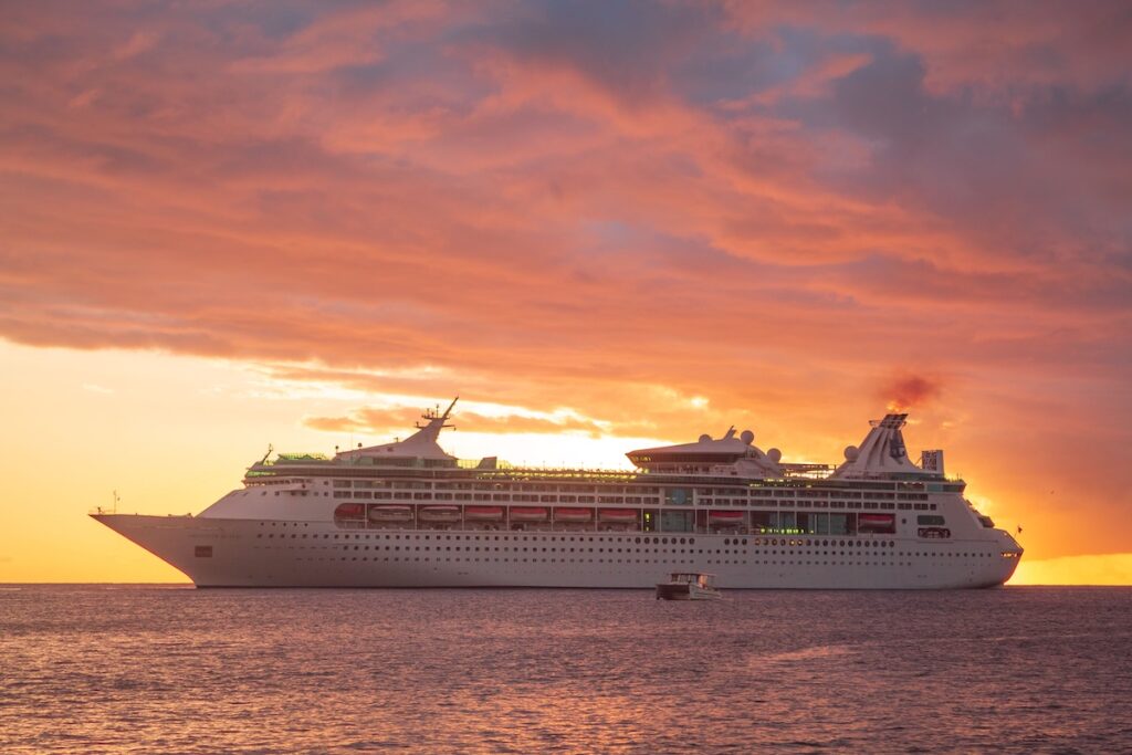 Cruise ship sailing at sunset under a calm, colorful sky