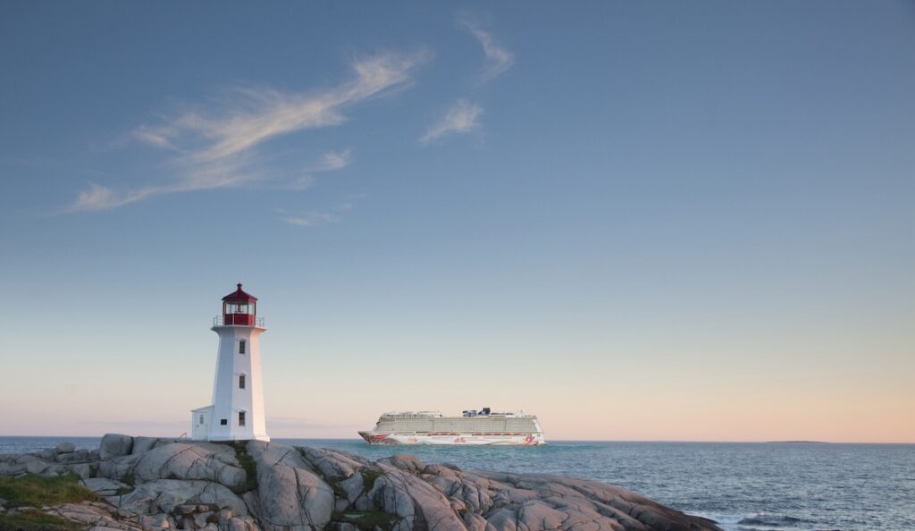 Cruise ship sailing calmly past a lighthouse at sunset.